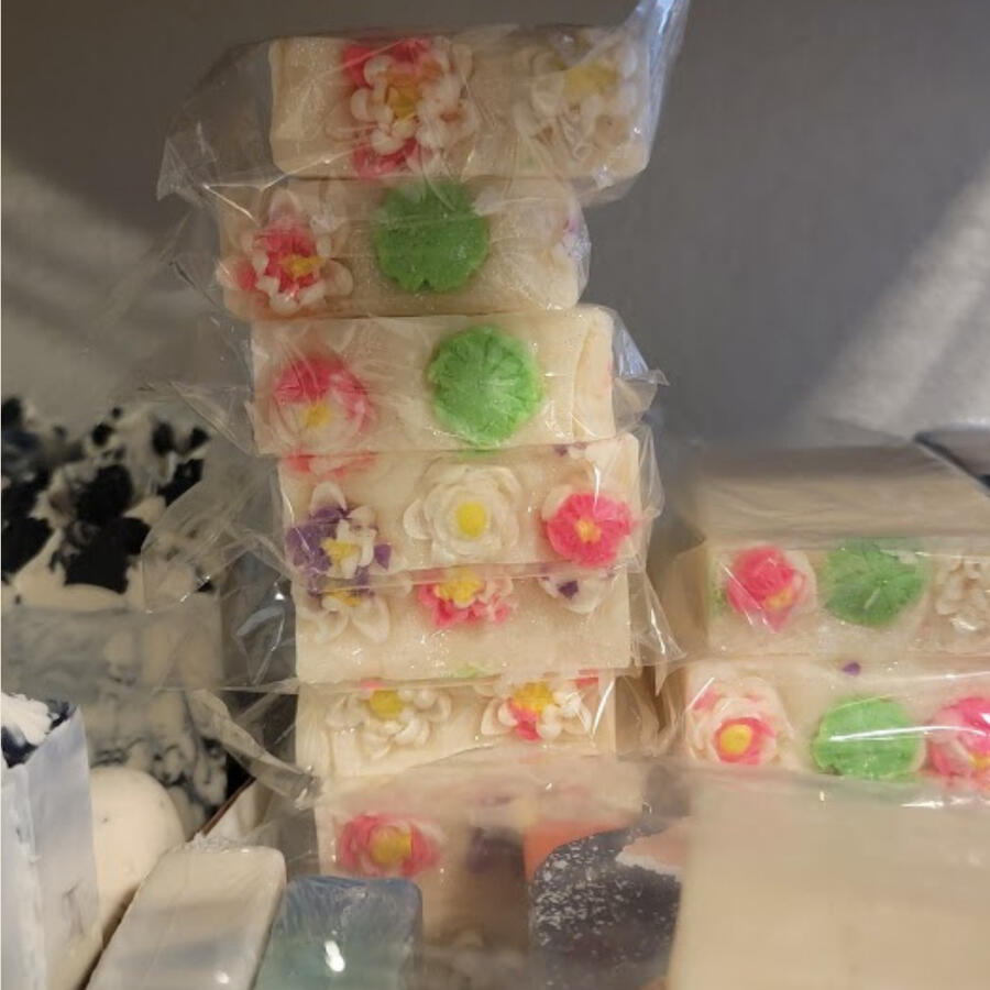 Soft marble soap topped with pink and white lotus flower embeds. A rectangular soap bar with delicate blush marbling and a carved lotus emblem on the front. Decorated with small, intricate water lily toppers in pink and white, evoking a serene and floral b